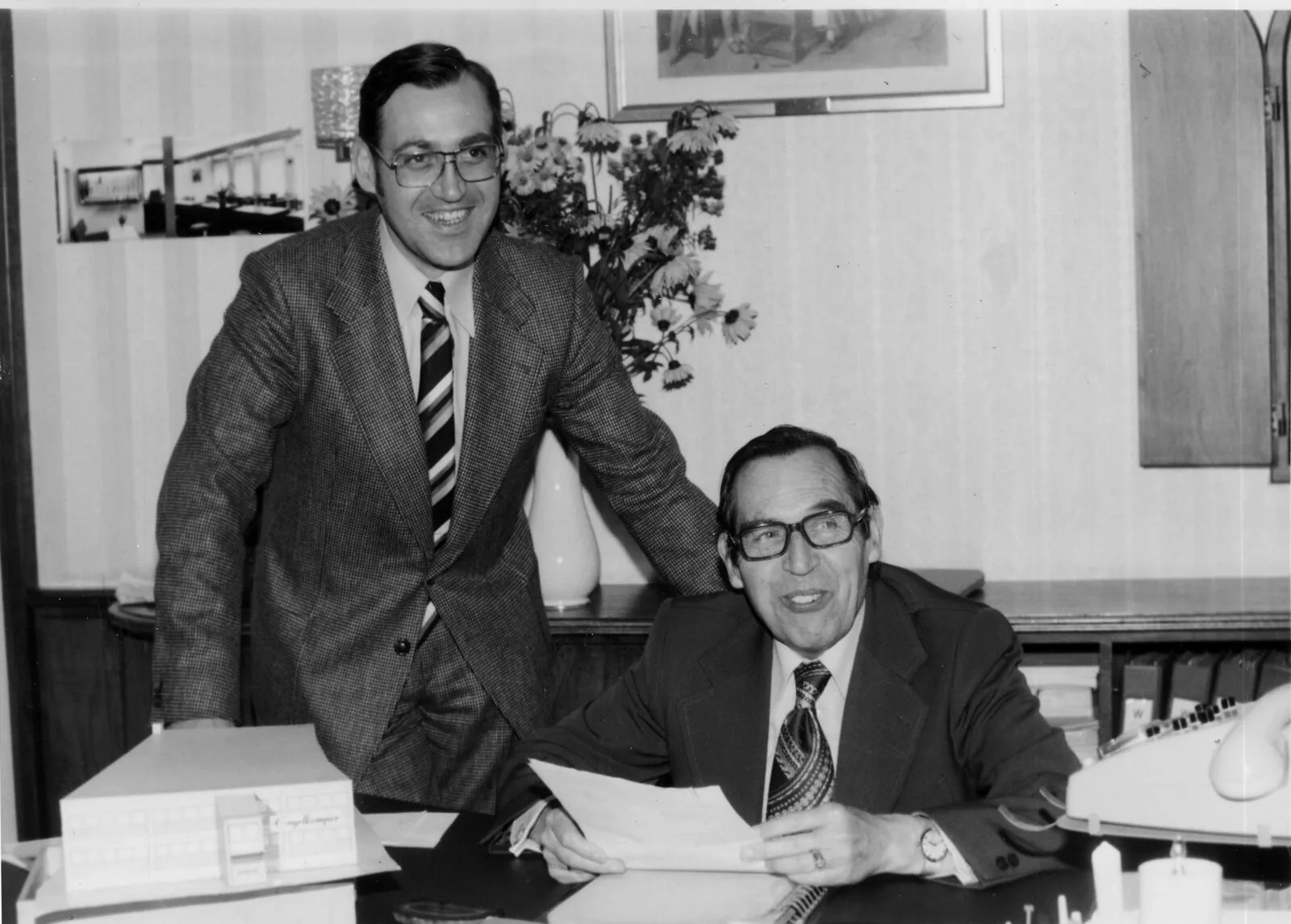 Rainer und Franz Abeler gemeinsam am Schreibtisch, im Vordergrund ein Architekturmodell des Firmengebäudes
